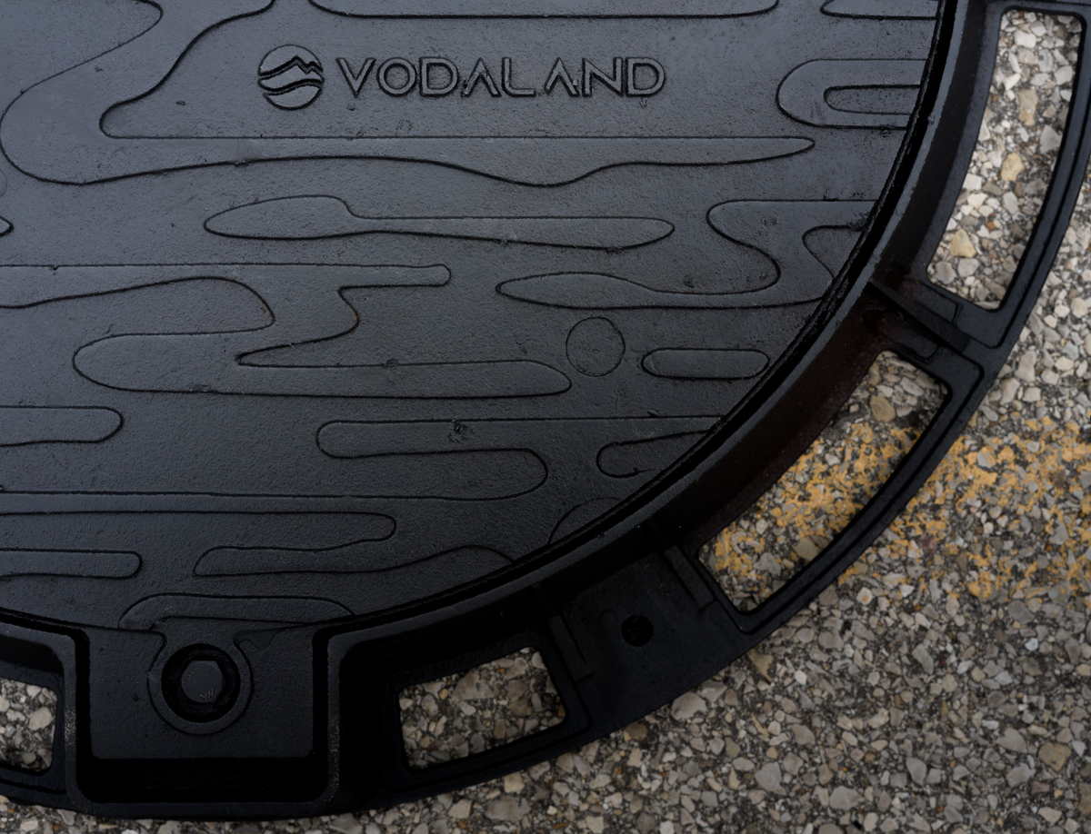 Black manhole cover with 'Vodaland' branding on a concrete surface